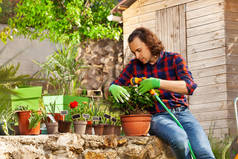 男子穿着园艺手套浇水盆栽花卉, 使用水管和喷雾喷嘴在后院