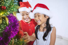 一个快乐的小女孩的照片, 装饰圣诞树与她的弟弟。在家中拍摄
