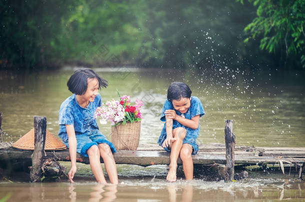 两个女孩坐在一起玩水在沼泽上的木桥, 亚洲孩子玩水 