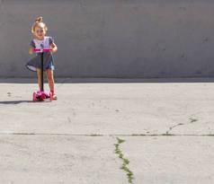可爱的孩子巧妙的溜冰鞋在一个粉红色的双轮摩托车在一个夏日晴朗的一天
