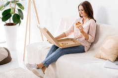 在家沙发上休息的年轻微笑的妇女吃比萨饼
