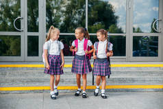 小学生的小学。有背包的女孩在户外的建筑附近。课程开始。秋天的第一天.