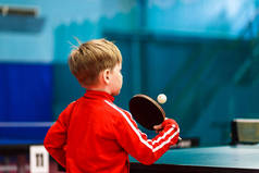 一个孩子在健身房打乒乓球, 一个孩子打网球。