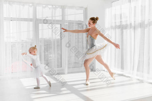 年轻华丽的芭蕾舞演员与她的小女儿在<strong>演播室</strong>跳舞。快乐的芭蕾舞演员与她的孩子女孩站在脚尖。母亲和女儿跳舞芭蕾