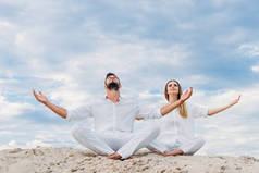 年轻夫妇的瑜伽冥想, 而坐在沙的沙丘上莲花姿势 (莲花)