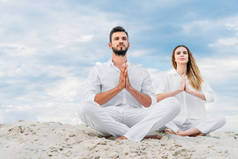 美丽的年轻夫妇练习瑜伽, 而坐在沙地上的莲花姿势 (莲花)
