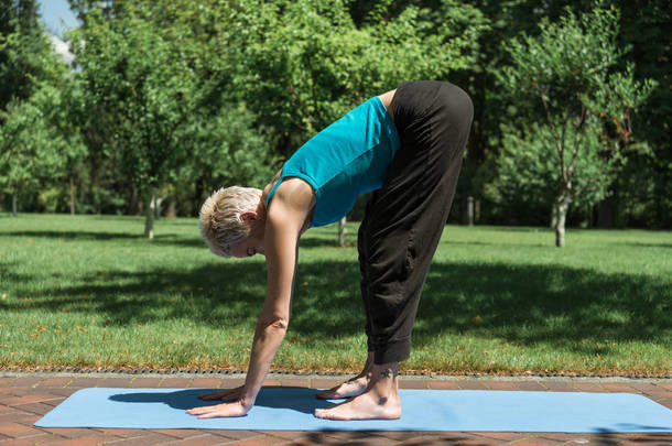 妇女练习<strong>瑜伽</strong>和做中途升降机姿势 (扭转 Uttanasana) 在<strong>瑜伽垫</strong>在公园