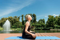 在公园附近的河边瑜伽垫上, 快乐女子练习瑜伽的侧面视图