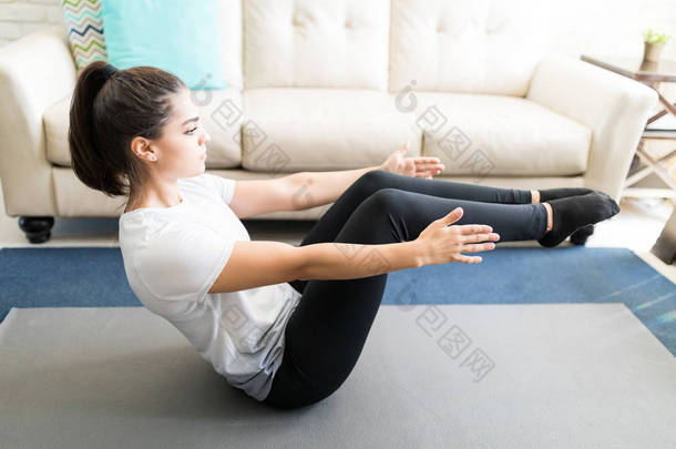 拉丁年轻妇女<strong>舒展</strong>和做小船瑜伽姿势在客厅里