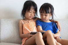 亚洲中国两个小姐妹在客厅沙发上使用平板电脑