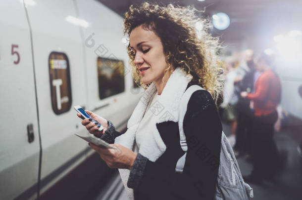 有吸引力的妇女与背包在中转<strong>平台</strong>上使用<strong>智能</strong>手机制作火车票的照片, 而地铁站的等待铁路列车.