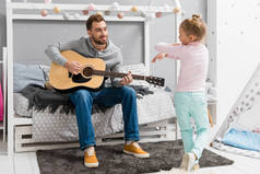 快乐的父亲在卧室里为女儿弹奏吉他, 而她在他面前跳舞