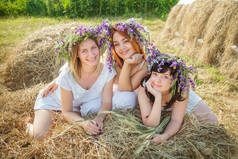 三个年轻漂亮的姑娘在白色礼服和花圈的干草堆旁的野花。在村子里的夏天