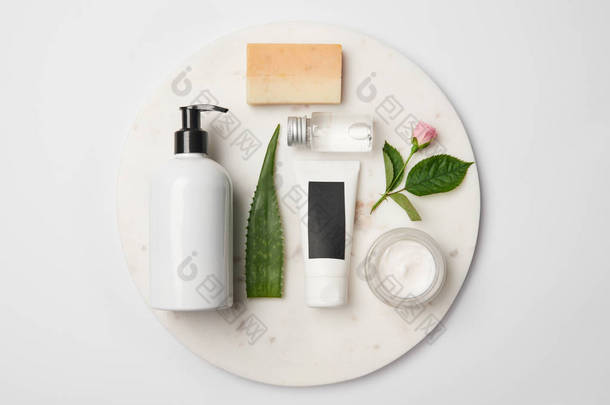 不同化妆品容器、肥皂、芦荟叶和玫瑰花在白色圆形表面的顶视图