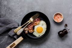 传统的英式早餐, 在旧灰色混凝土背景上的铸铁平底锅中煎蛋和培根。顶视图.
