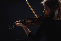 年轻的集中的妇女演奏大提琴与弓在黑暗中孤立的黑色 