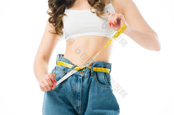 裁剪视图的妇女拿着测量带在大牛仔裤查出在白色, 减肥的概念
