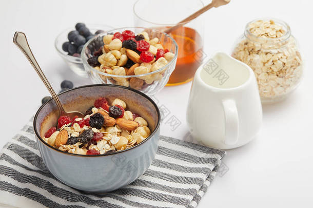 用燕麦片、坚果和浆果在白色桌子上用牛奶罐的条纹餐巾纸上的碗