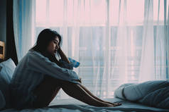 不愉快的美丽的亚洲妇女坐在床上看着悲伤和孤独