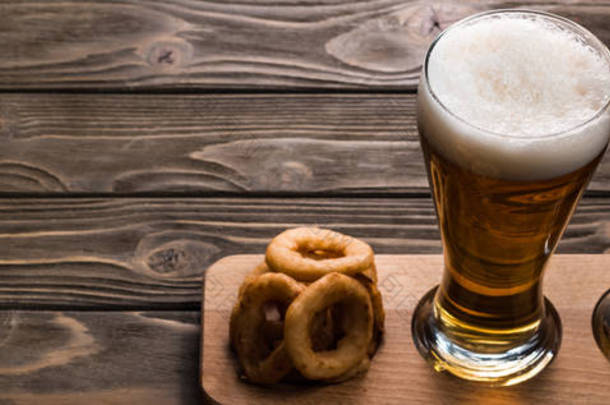 在木桌上煎洋葱圈附近用泡沫的<strong>黑啤</strong>酒和淡啤酒全景照片
