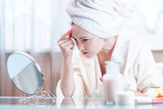 美丽不幸的年轻女子头上戴着毛巾, 检测到脸上的粉刺。皮肤卫生和护理的概念
