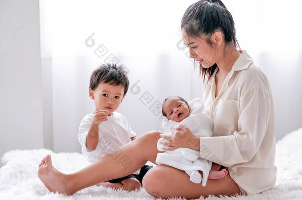 亚洲母亲把新生婴儿抱在腿上，和儿子一起坐在卧室的床上.