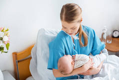 年轻母亲坐在病床上抱着可爱的新生儿的高视角