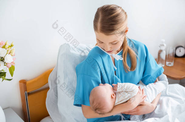 年轻母亲坐在<strong>病床</strong>上抱着可爱的新生儿的高视角