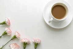 白杯中的咖啡, 粉红色和白色的康乃馨花在白色的桌子上。顶部视图.