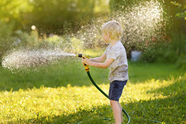 在阳光明媚的后院玩花园软管的滑稽小男孩。学前儿童玩喷雾水的乐趣。儿童夏季户外活动.