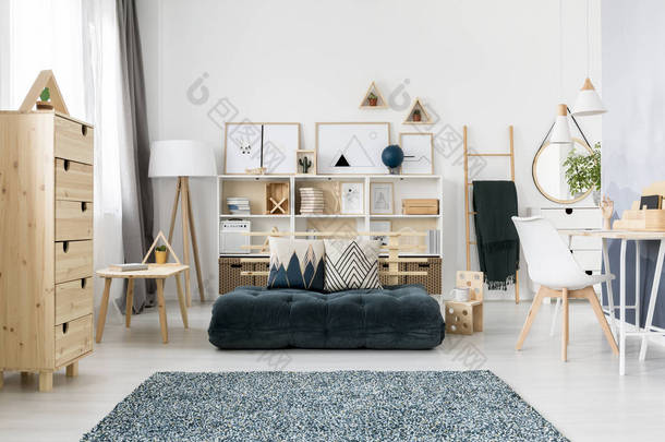 绿色折叠床垫和图案放置在斯堪的纳维亚客厅内部与木制家具和简单的画廊
