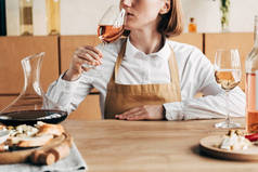 部分视图的侍酒师在围裙坐在桌边品尝葡萄酒