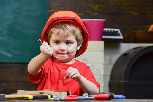 童年的概念。孩子梦想未来的建筑或建筑事业。男孩在橙色硬帽子或头盔, 学习室背景。男孩扮演建设者或修理工, 使用工具