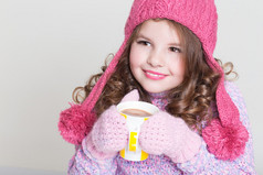 漂亮的孩子，在冬天帽子喝热巧克力，小姑娘在毛纺配件与杯茶或可可.