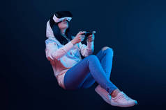 基辅，乌克兰 - 2019年4月5日：年轻女子在蓝色虚拟现实耳机中玩视频游戏时手持操纵杆的低角度视角  