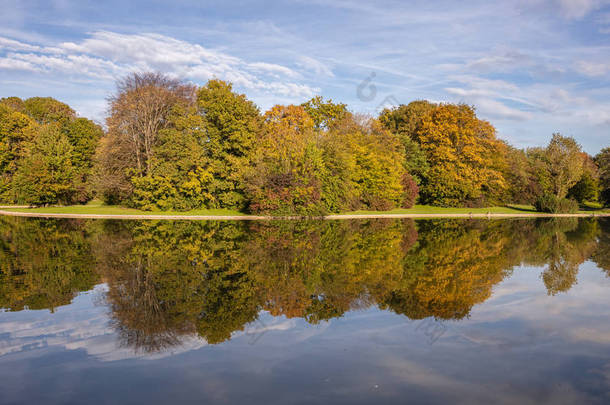 城市公园, 秋季, 慕尼黑, 德国。池塘里的草地、树木和倒影