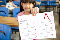 微笑的小女孩在教室里显示带有加号的试卷