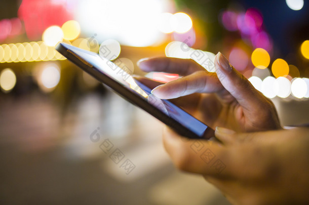 女人在街的夜晚光环境中使用她的手机号码