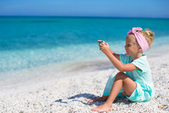 可爱的小女孩在电话里热带海滩拍照