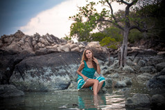 年轻漂亮的女人，坐在海边的一块石头上长绿松石穿着