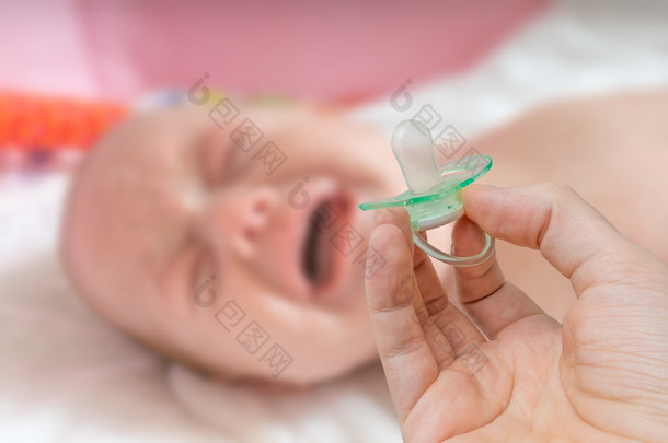 奶嘴在手和哭闹的婴儿，在背景中.