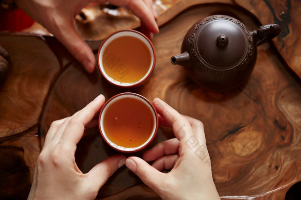 顶视图茶具茶道背景的木桌。女人和男人捧着一杯茶