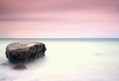 在安静的早晨在海上的浪漫气氛。从平静的波浪大海中伸出的巨砾。粉红色的地平线