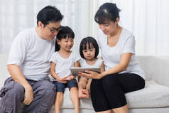 亚洲的中国父母和女儿在沙发上使用平板电脑