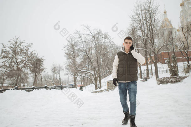 年轻英俊的男子，用电话的室外冬季肖像。他的夹克和背心摆在城市的街头，背景的杉树上的美丽少年.