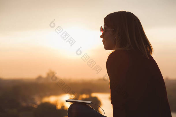 年轻女人享受夕阳听在智能手机上的音乐