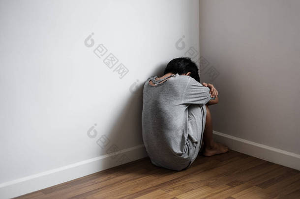 沮丧的年轻人独自一人坐在角落里的房间、 悲伤、 沮丧和生活问题的概念
