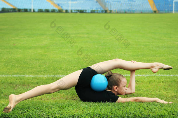 在绿色草地上球的年轻女孩体操运动员