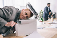 过度劳累的年轻商人在办公室里靠复印机