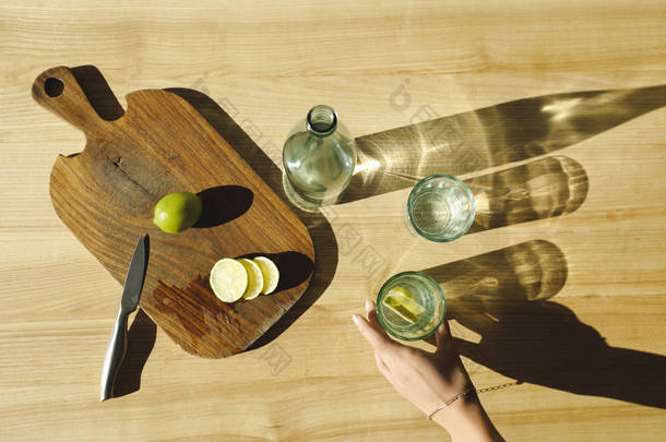 妇女在木桌上放杯柠檬水的裁剪图像
